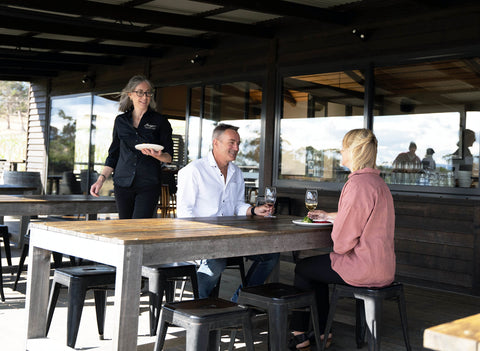 A couple outdoor dining at the wooden picnic tables on Bangor's covered and heated deck, Bangor Vineyard Shed near Hobart, Tasmania