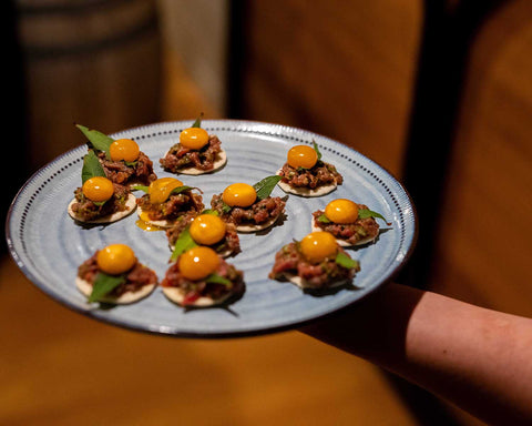 Platter of small appetizers with yellow toppings held by a person.