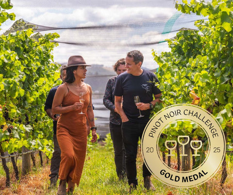 Walking through Bangor vineyard with a Pinot Noir Challenge gold medal logo.